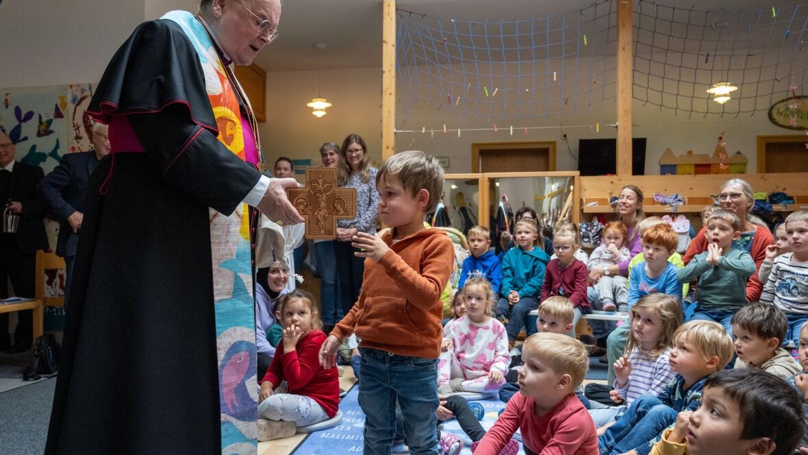 Bischof Bertram überreicht einem Kind das Ulrichskreuz.
